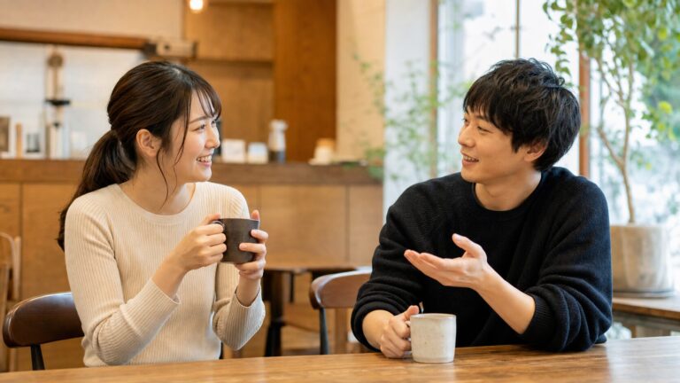 カフェで男友達と楽しそうに話す女性と、その様子を少し気にしている彼氏の写真