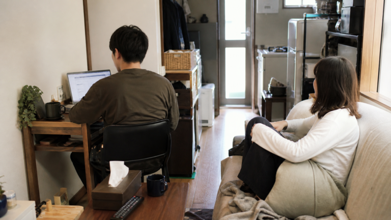 1LDKの部屋で、デスクで作業する人と少し離れた場所でくつろぐ人が同じ空間で過ごしている同棲の様子