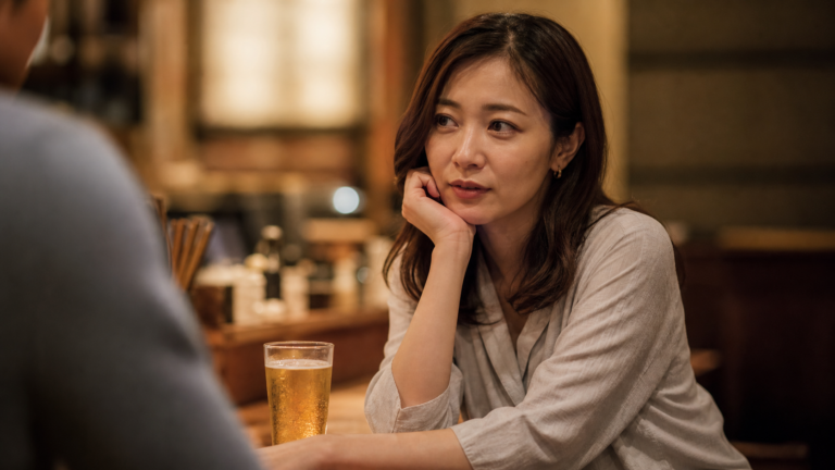 居酒屋の個室で既婚男性と向き合い、グラスを前に複雑な表情を浮かべる女性の写真