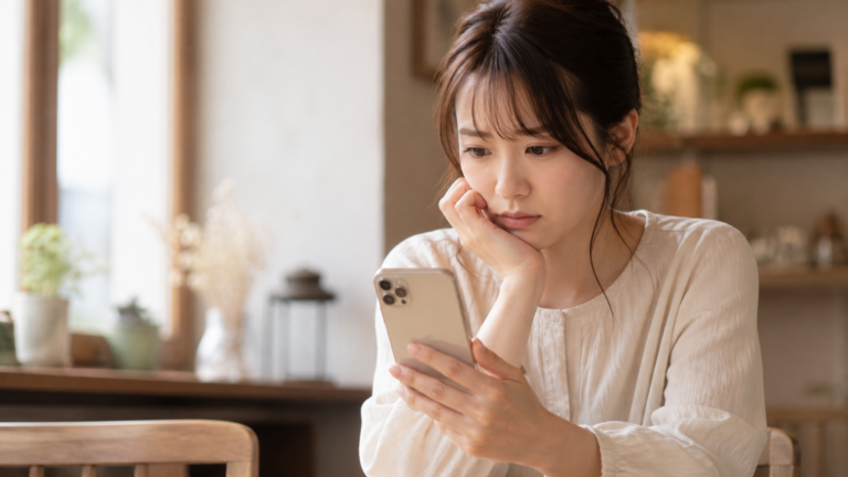 スマートフォンでマッチングアプリのメッセージ画面を見つめ、返信が来ず不安そうな表情の女性の写真