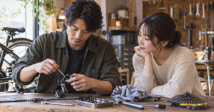 作業中の手元を見せながらそっと隣に座る男性と、気になる表情で見つめる女性の写真