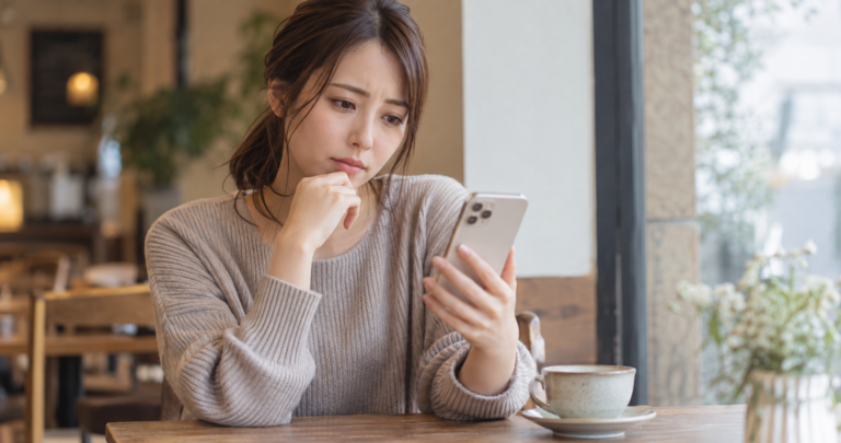 スマートフォンでLINEのメッセージを気にしながら考え込む女性の写真
