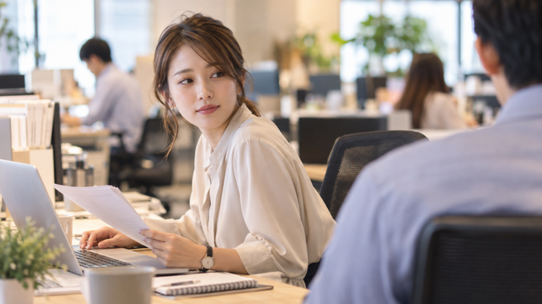 オフィスのデスクで隣の席の同僚をさりげなく気にする女性社員の横顔