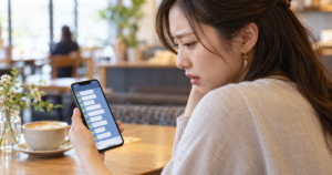 猛アタックされて戸惑いながらスマートフォンのLINE画面を見つめる女性の写真