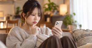 スマホを気にしながら不安な表情をしている女性のイメージ写真